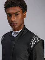 Mono Alpinestars Hypertech V3, traje de automovilismo Black Dark Shadow, primer plano de modelo masculino, logotipos plateados en los hombros, cuello alto con camiseta blanca Alpinestars de cuello falso, equipo de protección profesional para automovilismo