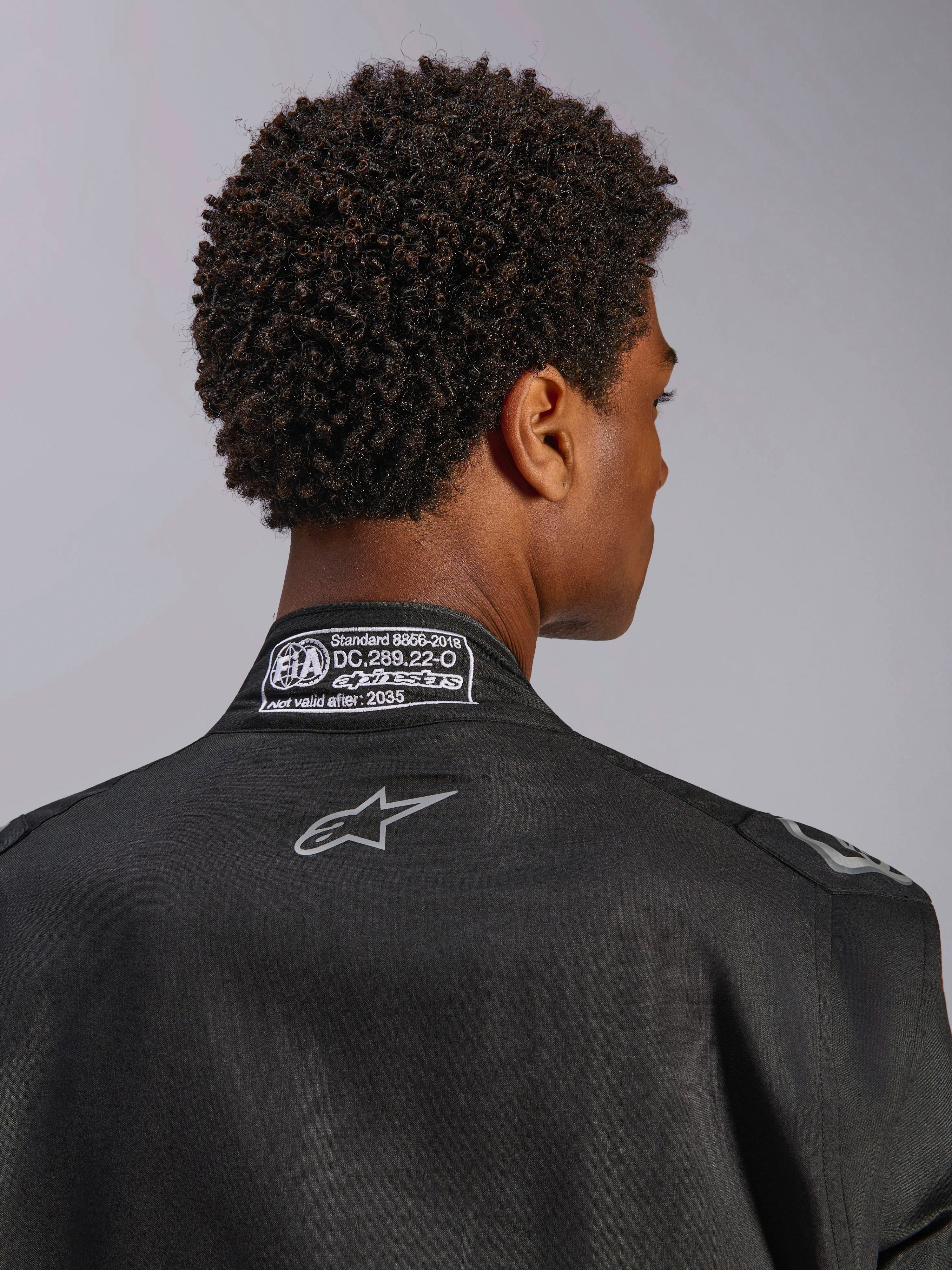 Mono Alpinestars Hypertech V3, Black Dark Shadow, primer plano de la vista trasera del cuello con etiqueta de certificación FIA 8856-2018 y logotipo en la espalda, traje de carreras profesional ligero con corte atlético