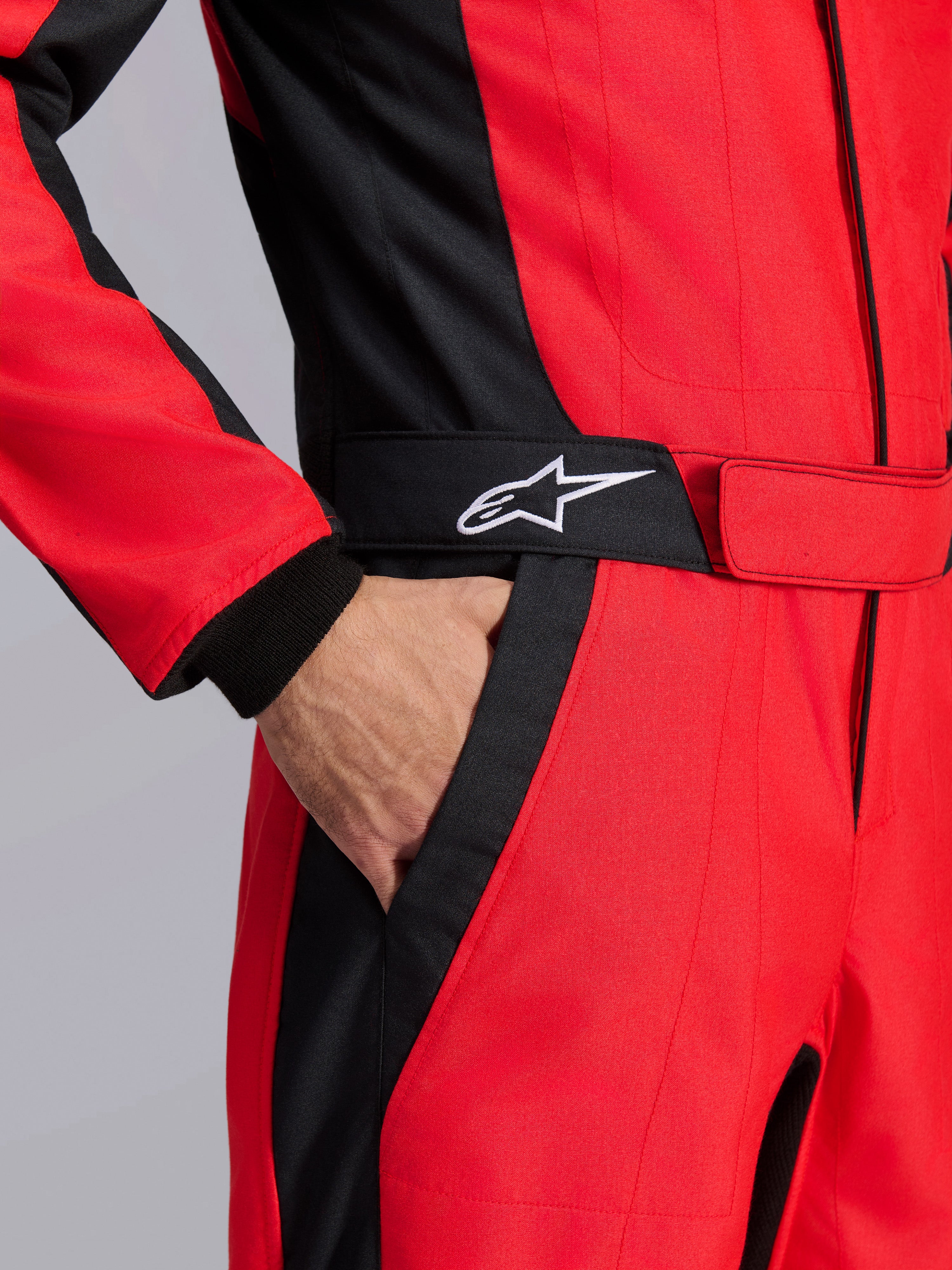 Alpinestars GP Pro Comp V2 FIA Racing Suit, Red and Black, close-up of the waist area showing a hand in the pocket, featuring a black belt with a white star logo and structured panels for auto racing