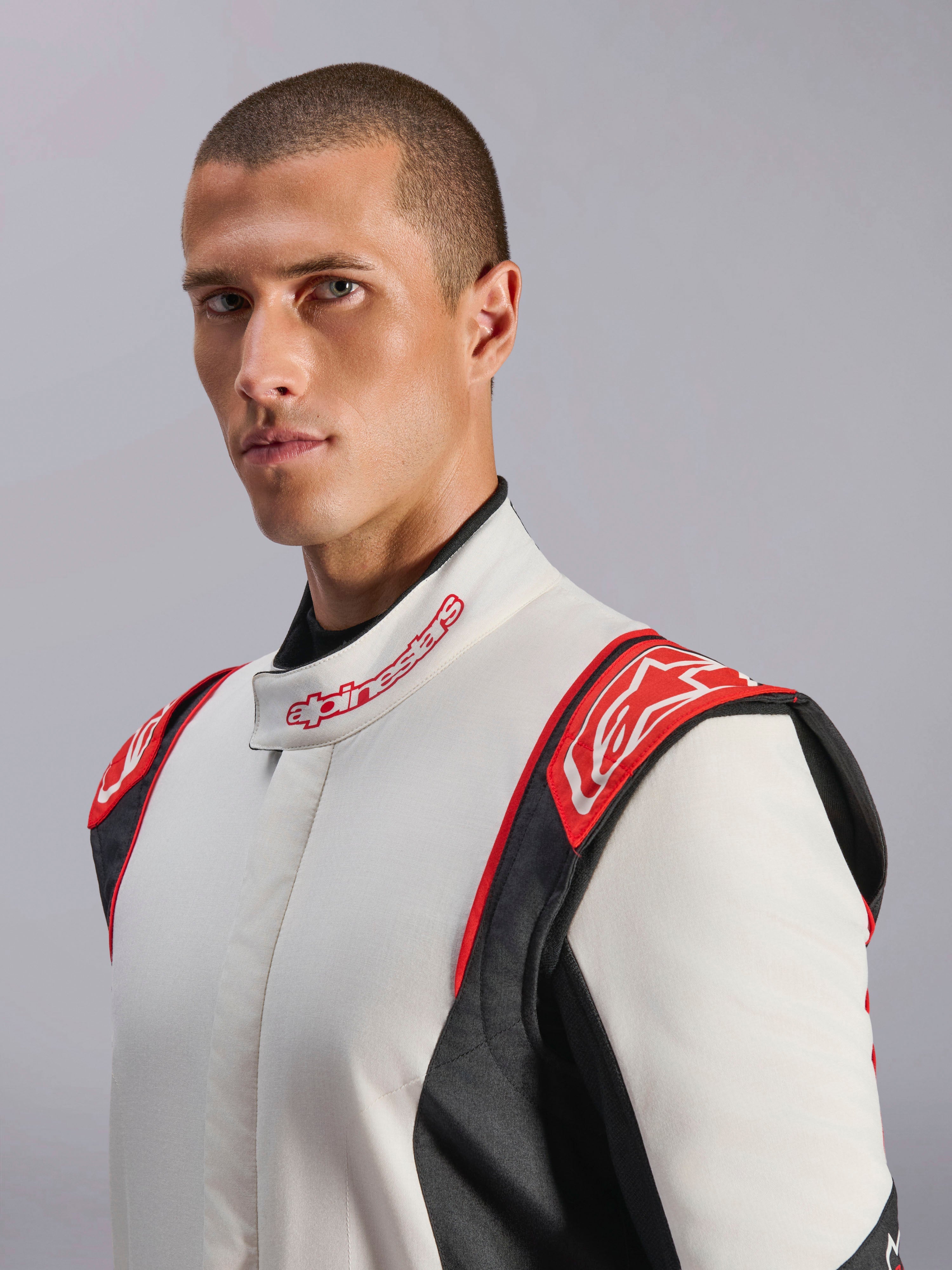 Mono Alpinestars GP Tech V4, mono de automovilismo, blanco, negro y rojo, lucido por un modelo, con paneles rojos en los hombros con el logotipo de Alpinestars, torso blanco con paneles laterales negros y cuello con marca, equipo profesional de automovilismo