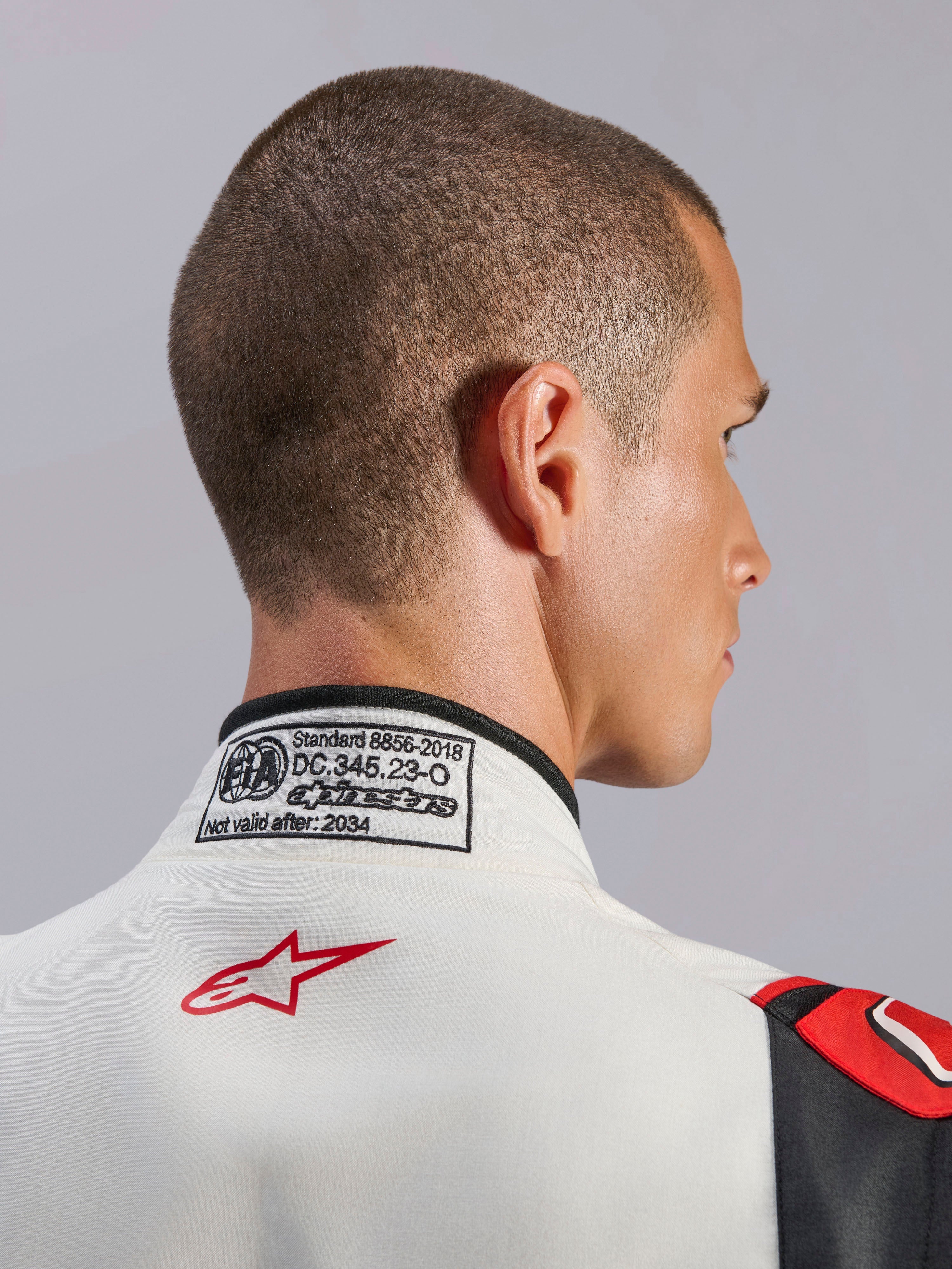 Mono Alpinestars GP Tech V4, traje de automovilismo en blanco, negro y rojo, primer plano de la parte trasera del cuello que muestra la etiqueta de certificación FIA 8856-2018 y el logotipo de la estrella roja, equipo de seguridad profesional para automovilismo