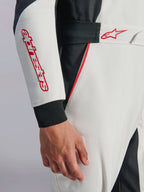 Mono Alpinestars GP Tech V4, mono de automovilismo en blanco, negro y rojo, primer plano de la manga y la cintura con el nombre y el logotipo de la estrella de Alpinestars en rojo, cintura elástica con cierre de velcro y ribetes rojos sobre tejido técnico blanco y negro