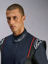 Retrato de primer plano de un modelo que viste el mono Alpinestars GP Tech V4, traje de automovilismo en azul marino, negro y rojo, con la marca Alpinestars en el cuello alto y charreteras estructuradas en los hombros.