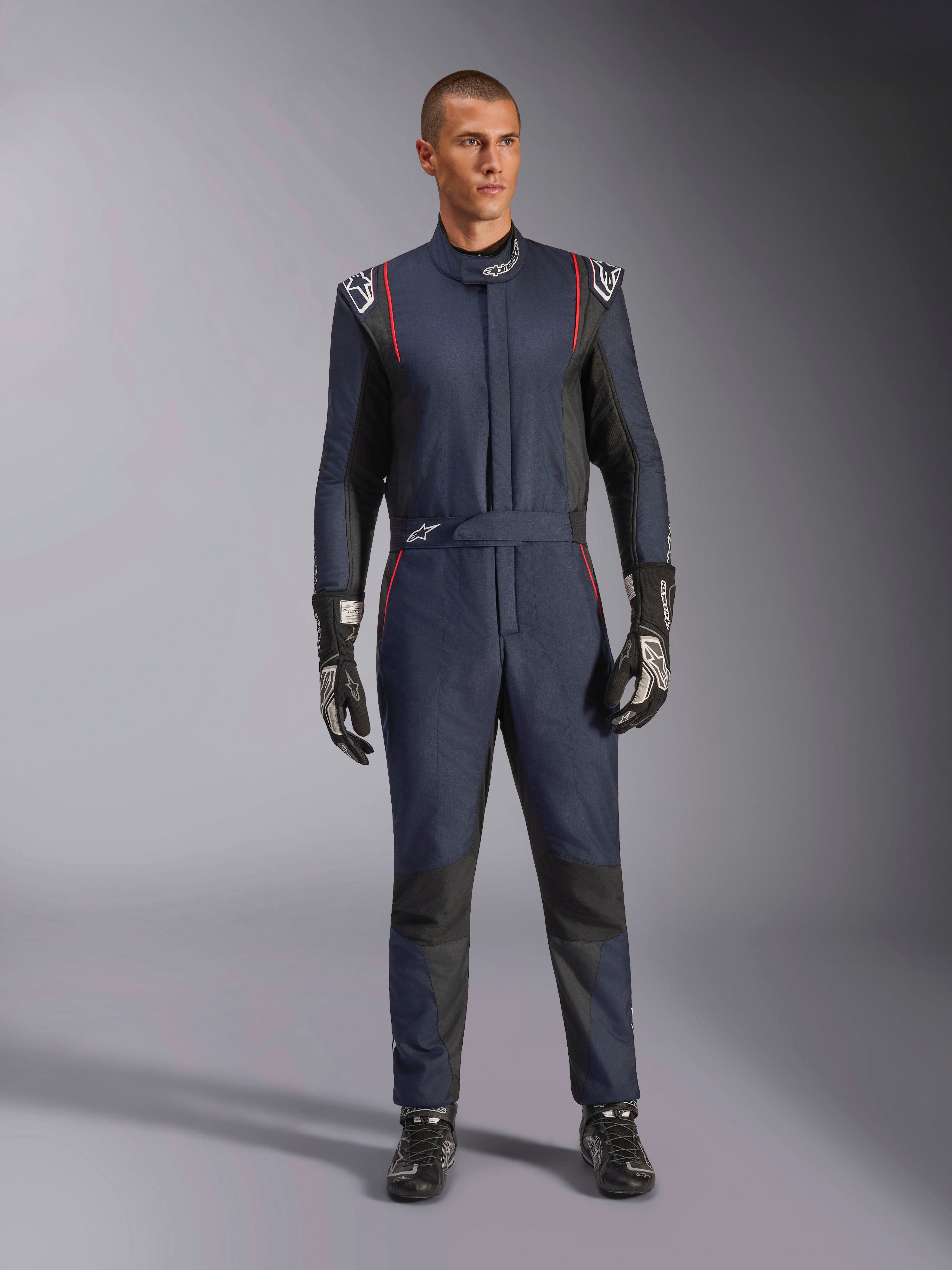 Mono Alpinestars GP Tech V4, traje de automovilismo profesional en azul marino y negro con ribetes rojos, equipamiento de carreras de una sola pieza con certificación FIA, usado con guantes y calzado de carreras negros, indumentaria para piloto de automovilismo
