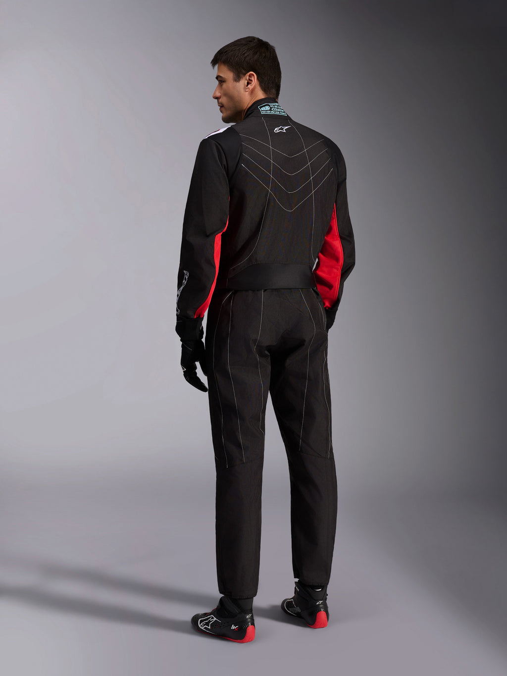 Mono Alpinestars KMX-9 V3, negro, rojo y blanco, mono de karting de una pieza visto desde atrás, con costuras geométricas blancas en la espalda y detalles rojos en las mangas, usado con guantes de carreras negros y botas de karting