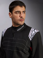 Mono Alpinestars KMX-9 V3, mono de karting negro llevado por un modelo masculino, primer plano del pecho y los hombros con logotipos blancos en el cuello y las hombreras, con costuras decorativas blancas y un diseño profesional para deportes de motor