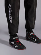 Alpinestars KMX-9 V3 Suit, mono de karting, negro, rojo y blanco, vista detallada de la parte inferior de las piernas y botas de karting, marca Alpinestars blanca en el lateral, calzado negro con cordones rojos y detalles blancos, equipamiento profesional de carreras