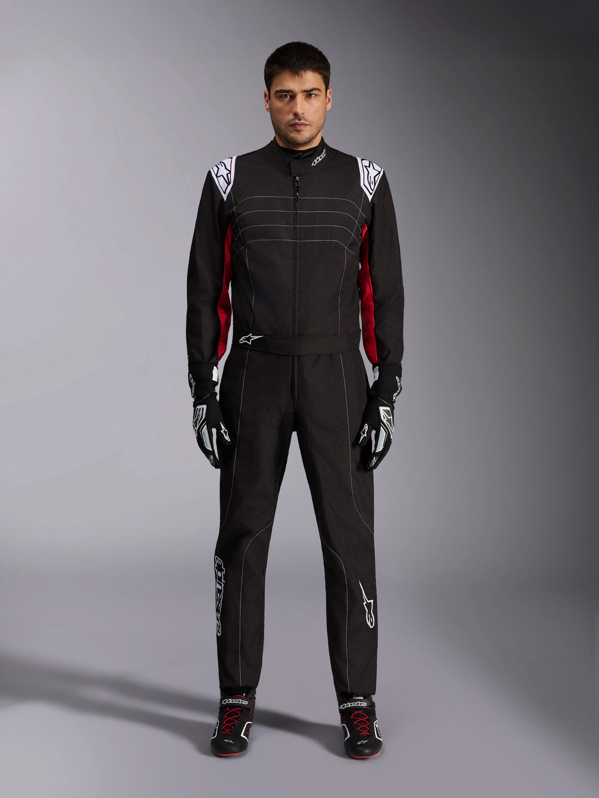 Mono de karting Alpinestars KMX-9 V3 en negro, rojo y blanco, vista frontal de cuerpo completo de un modelo luciendo el mono de una pieza con guantes y calzado de competición coordinados, con logotipos blancos de Alpinestars en los hombros y detalles en rojo.