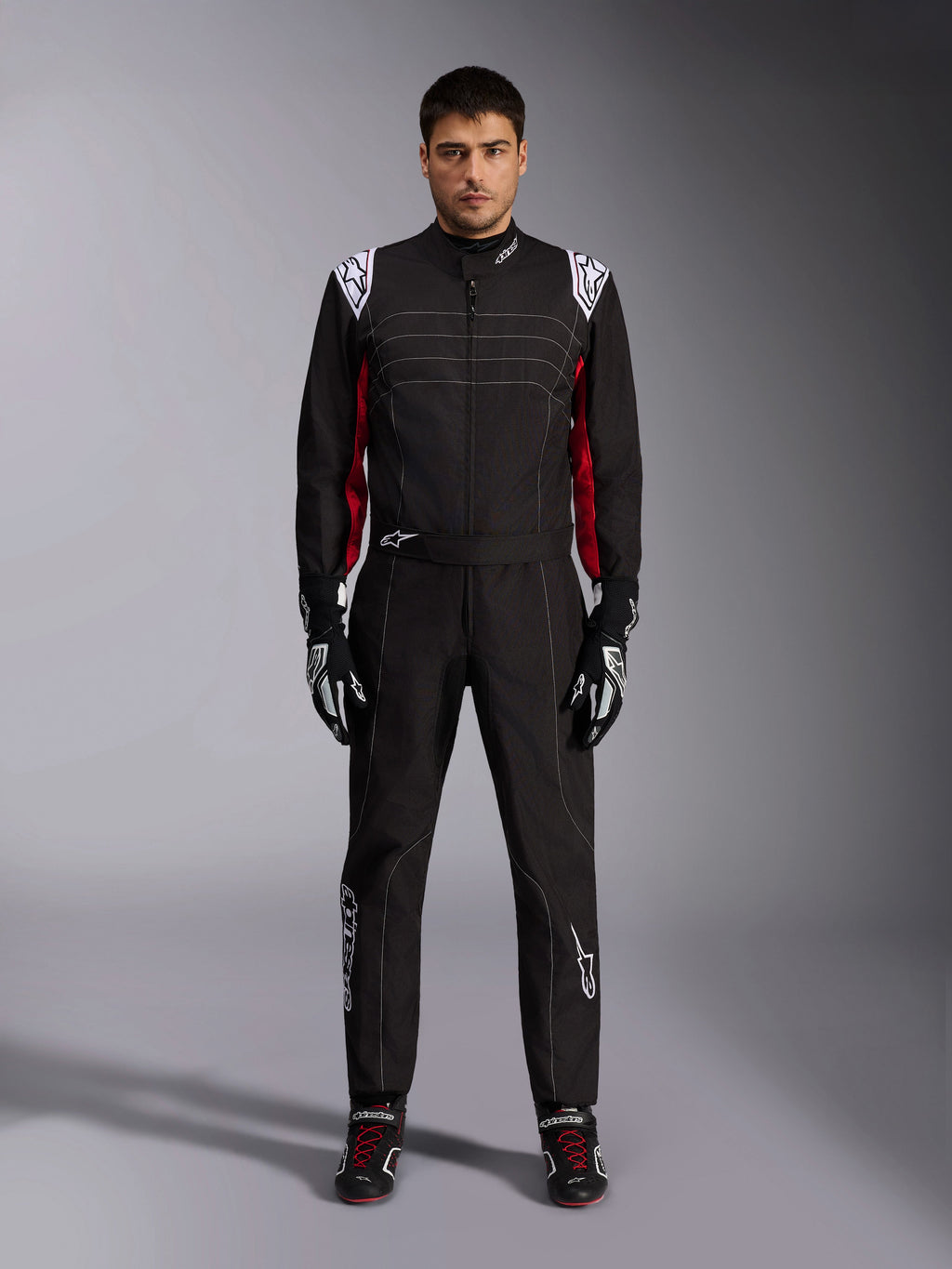 Mono de karting Alpinestars KMX-9 V3 en negro, rojo y blanco, vista frontal de cuerpo completo de un modelo luciendo el mono de una pieza con guantes y calzado de competición coordinados, con logotipos blancos de Alpinestars en los hombros y detalles en rojo.
