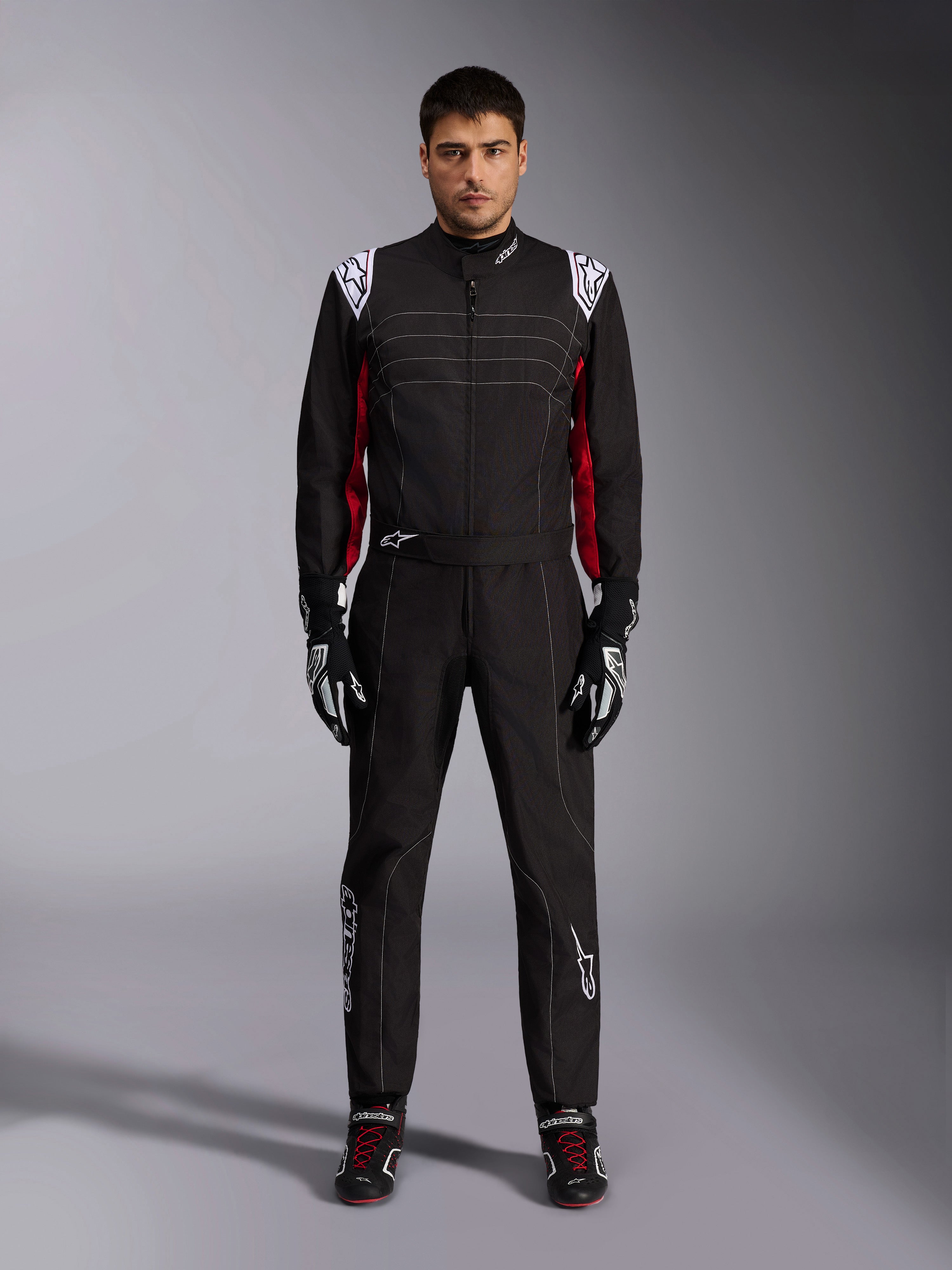 Mono de karting Alpinestars KMX-9 V3 en negro, rojo y blanco, vista frontal de cuerpo completo de un modelo luciendo el mono de una pieza con guantes y calzado de competición coordinados, con logotipos blancos de Alpinestars en los hombros y detalles en rojo.