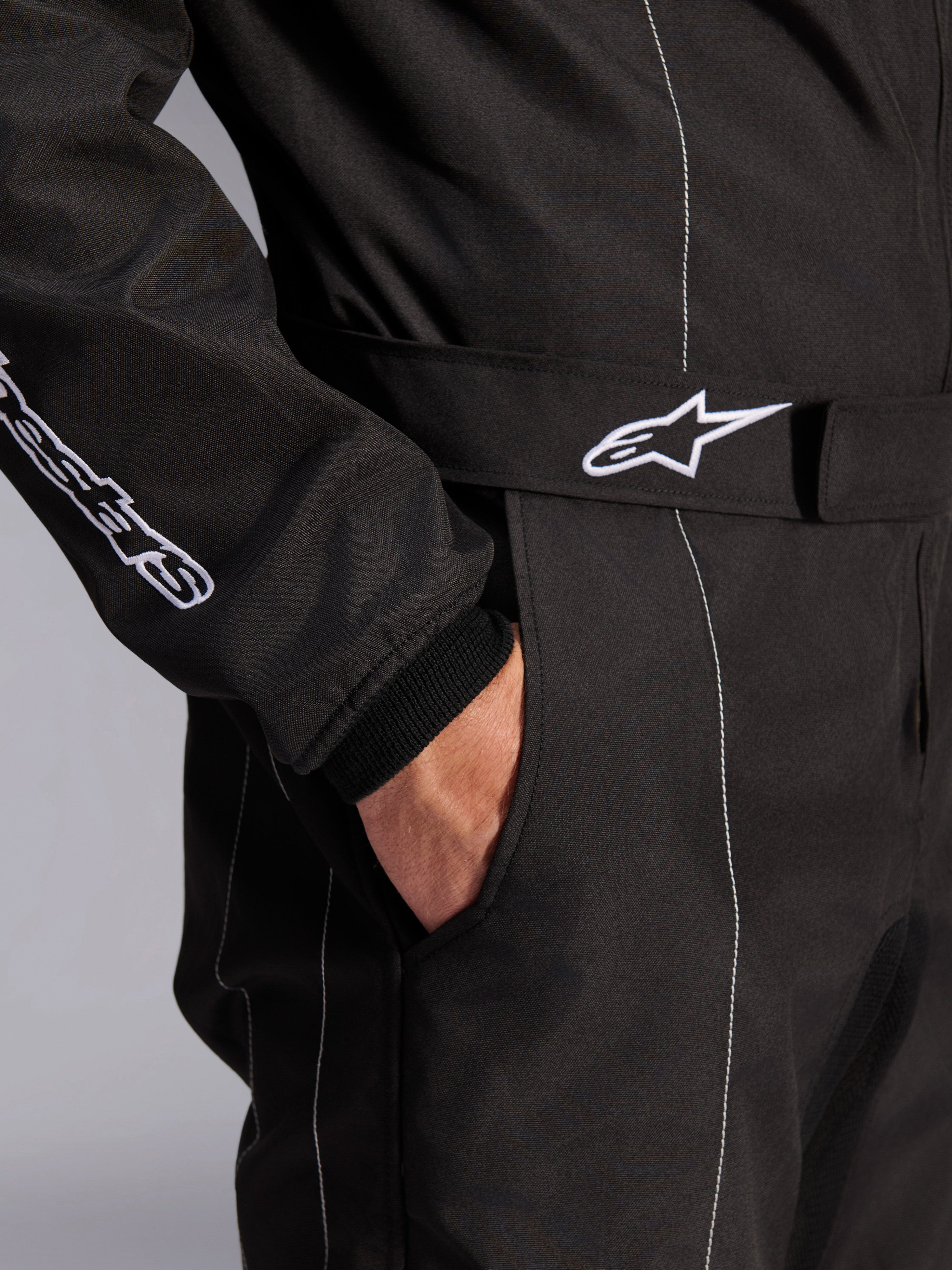 Mono Alpinestars KMX-9 V3, negro y blanco, vista de cerca de la cinturilla ajustable con logotipo bordado, bolsillo lateral, costuras blancas en contraste sobre tejido negro, detalle técnico del mono de karting
