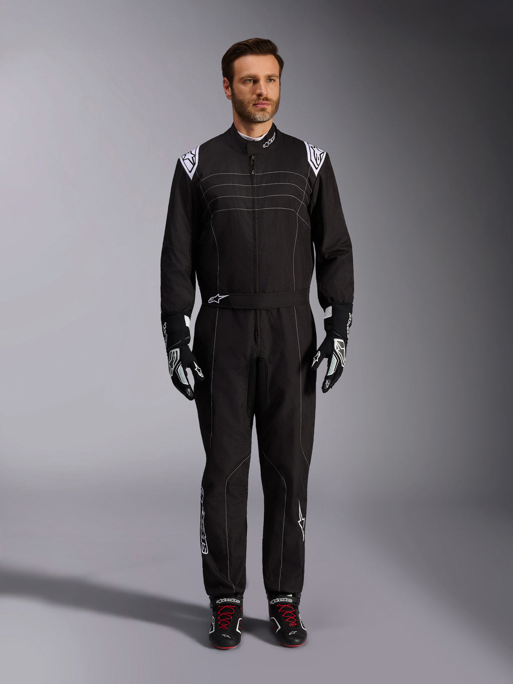 Mono Alpinestars KMX-9 V3, traje de karting negro y blanco, vista de cuerpo completo en un modelo, con logotipos y detalles blancos en los hombros, combinado con guantes de carreras en blanco y negro y calzado negro con cordones rojos, ajuste atlético-regular para equipamiento de karting profesional.
