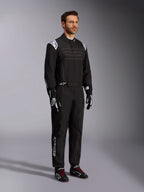 Alpinestars KMX-9 V3 Karting Suit, negro y blanco, modelo masculino vistiendo un mono de carreras completo con el logotipo de Alpinestars blanco en las hombreras, combinado con guantes de carreras negros y blancos y zapatillas de karting negras con cordones rojos, toma de estudio que muestra el perfil frontal y lateral
