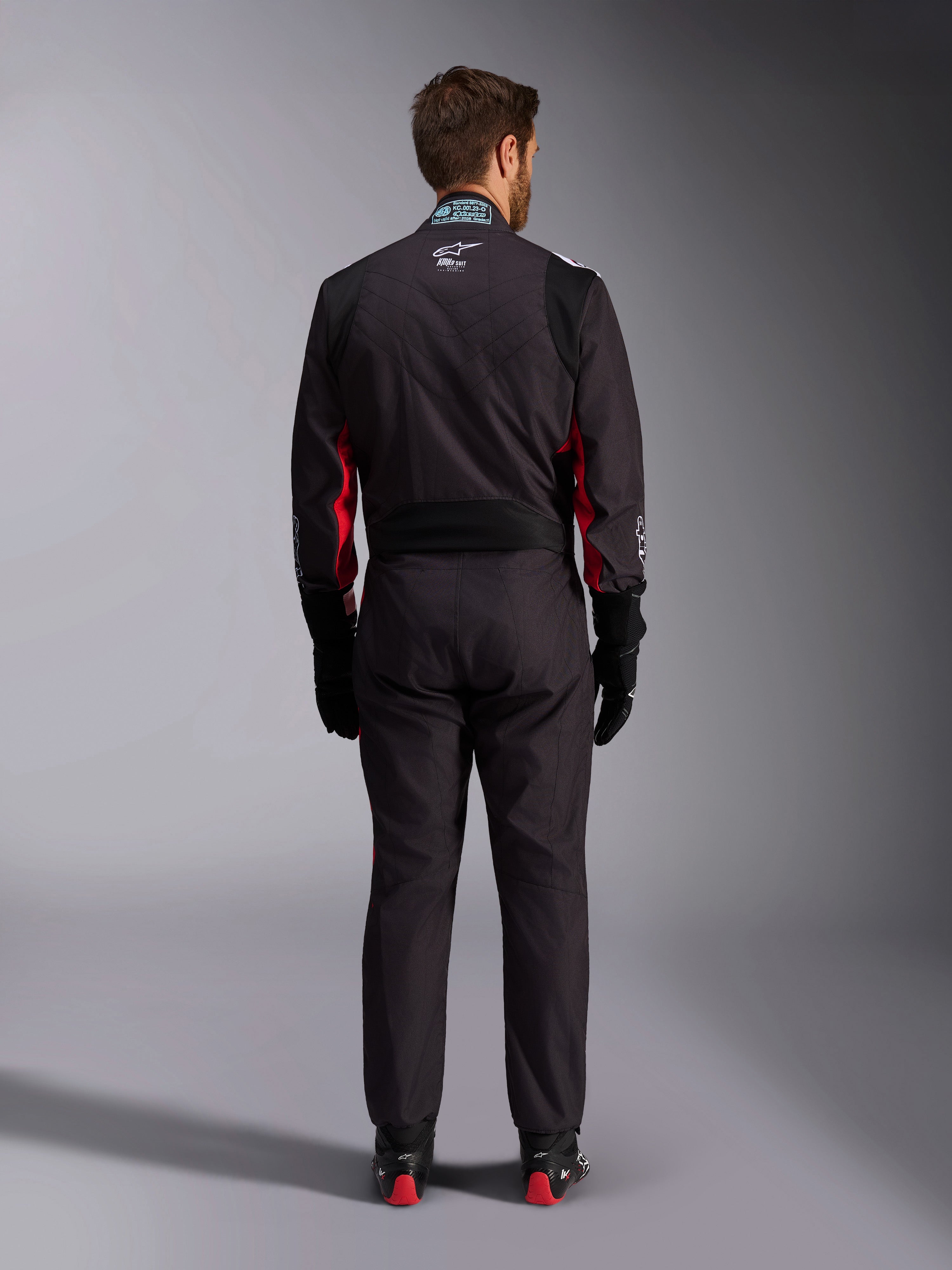 Mono Alpinestars KMX-9 V3 Graphic 3, traje de karting, negro y rojo, vista posterior con el panel elástico lumbar y la etiqueta de certificación FIA en el cuello, combinado con guantes de carreras negros y botas con detalles rojos