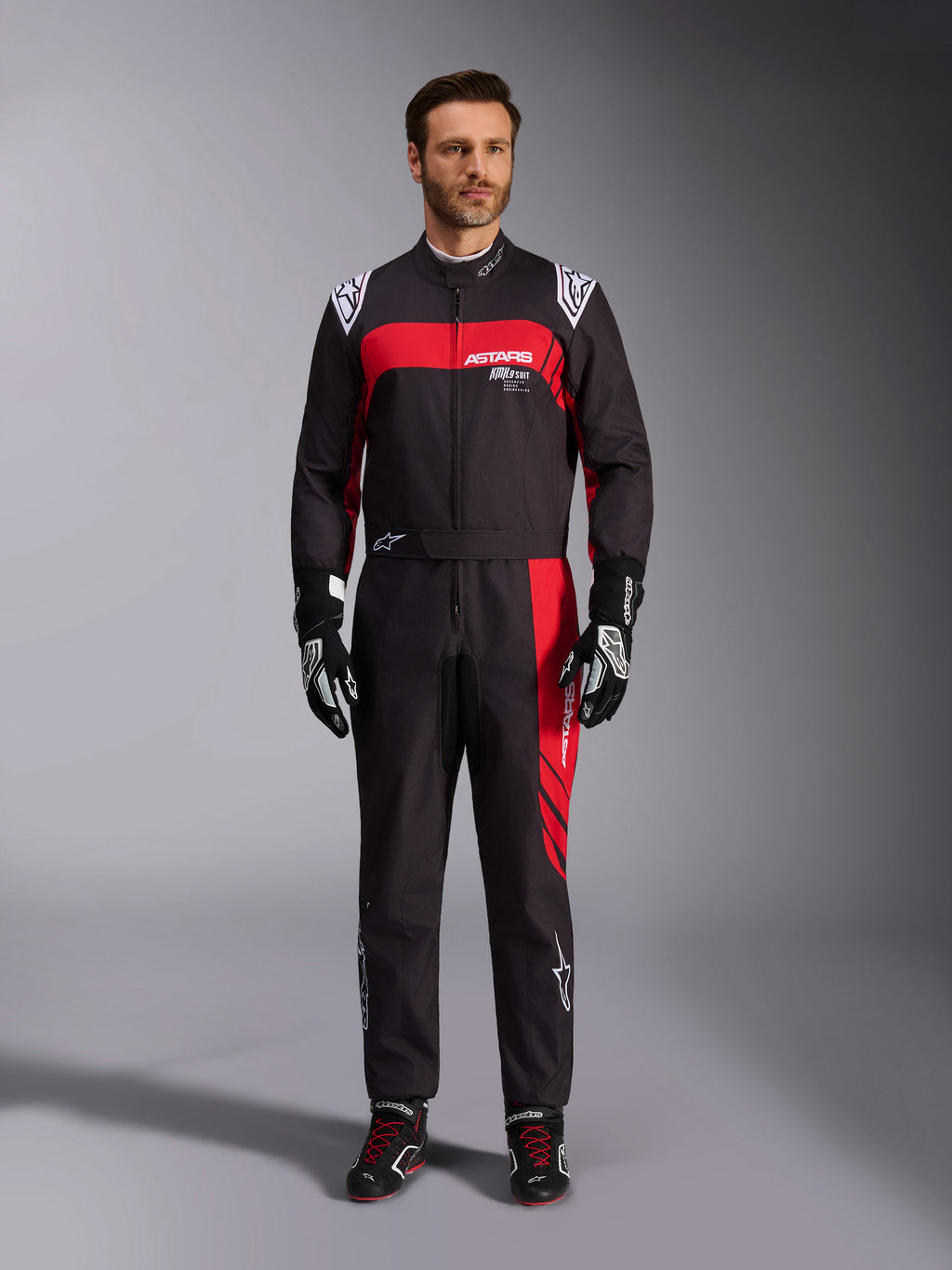 Mono Alpinestars KMX-9 V3 Graphic 3, mono de karting, negro y rojo, vista frontal de cuerpo completo en modelo, con paneles gráficos en rojo y logotipos blancos, combinado con guantes y calzado de competición negros, equipamiento profesional de automovilismo.