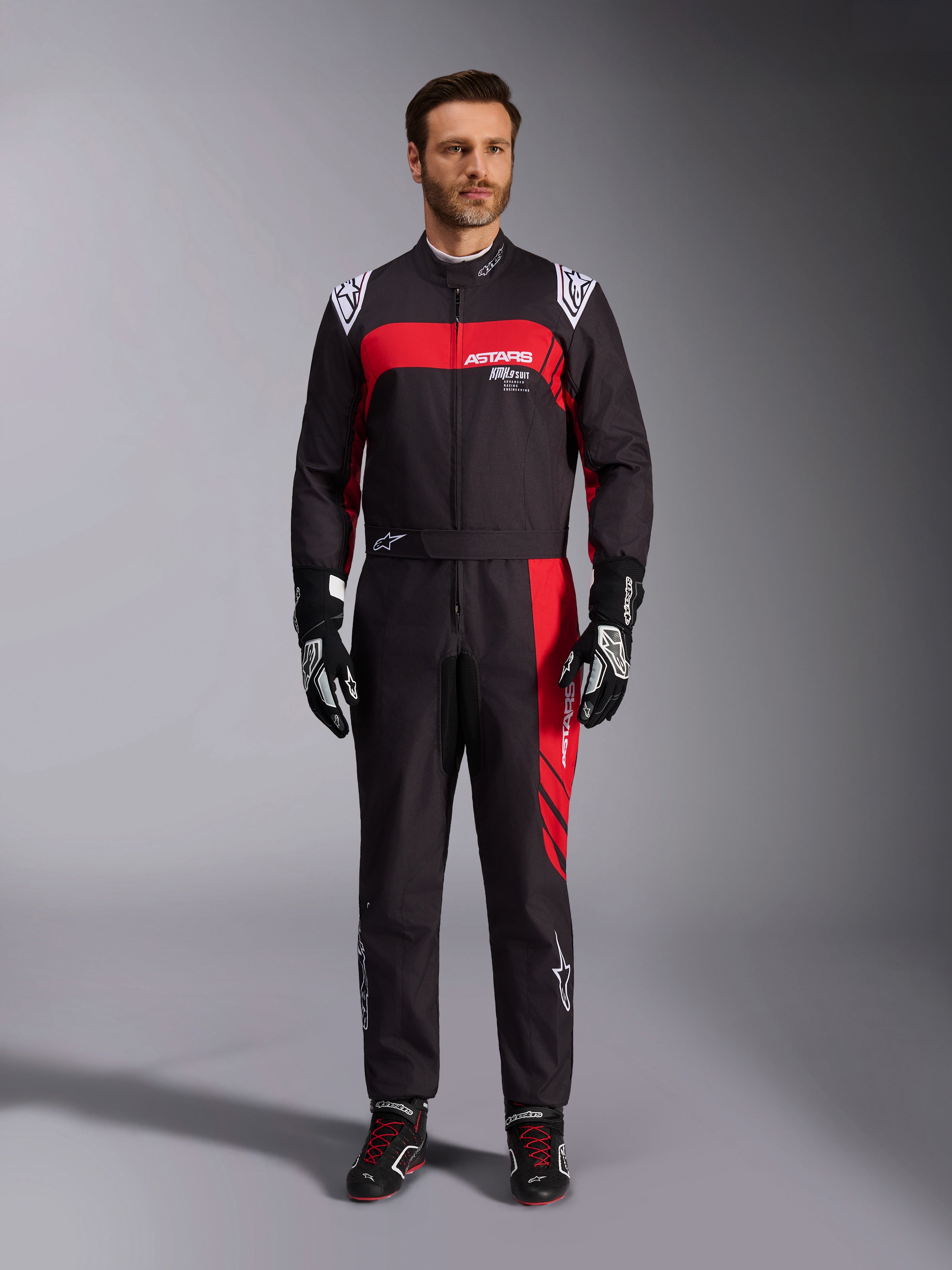 Mono Alpinestars KMX-9 V3 Graphic 3, mono de karting, negro y rojo, vista frontal de cuerpo completo en modelo, con paneles gráficos en rojo y logotipos blancos, combinado con guantes y calzado de competición negros, equipamiento profesional de automovilismo.