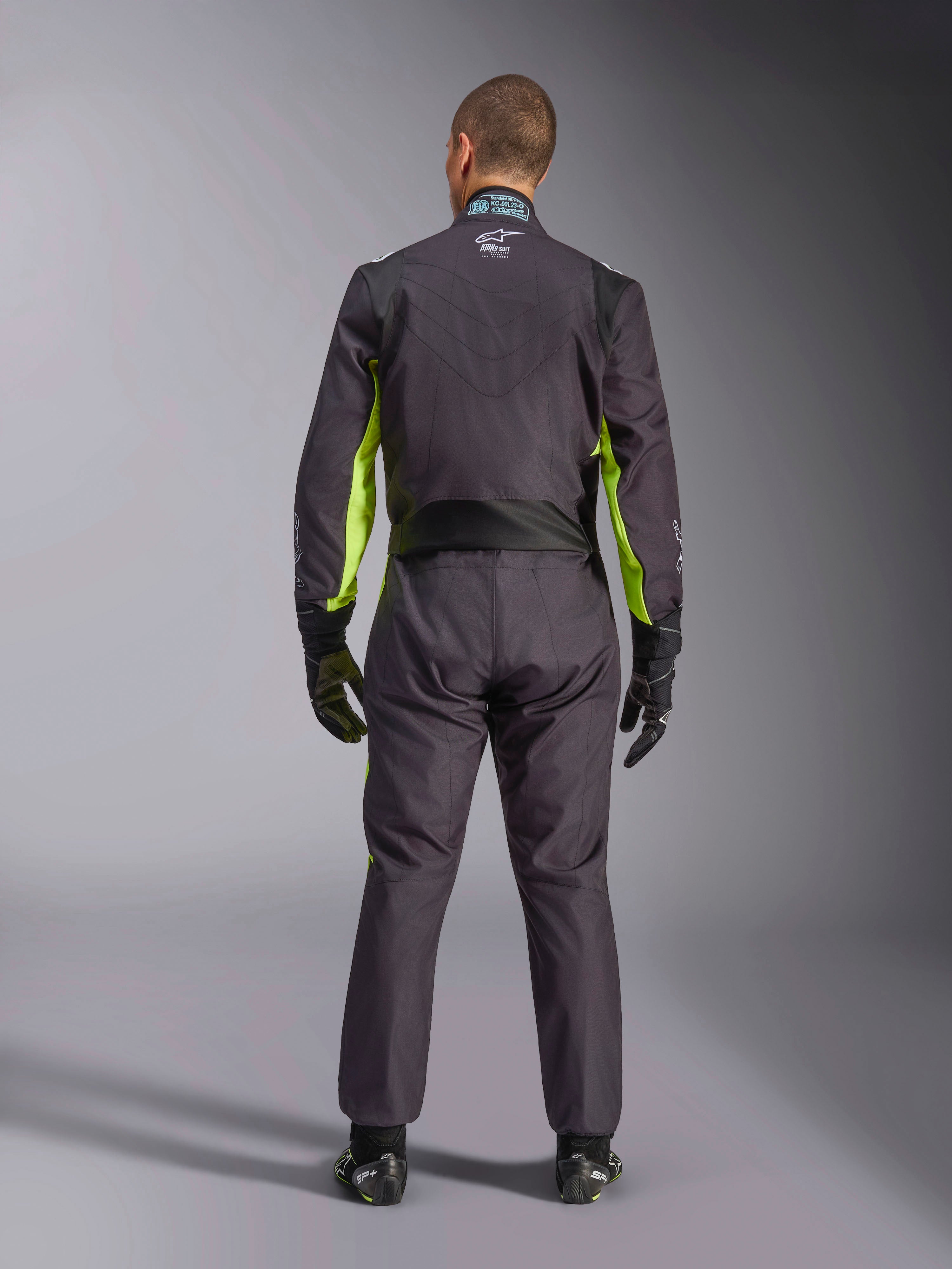 Vista posterior de cuerpo completo de una persona con el Traje Alpinestars KMX-9 V3 Graphic 3, mono de karting en color negro y amarillo flúor, que muestra los paneles elásticos ergonómicos en la espalda y los hombros, combinado con guantes de carreras negros y calzado.