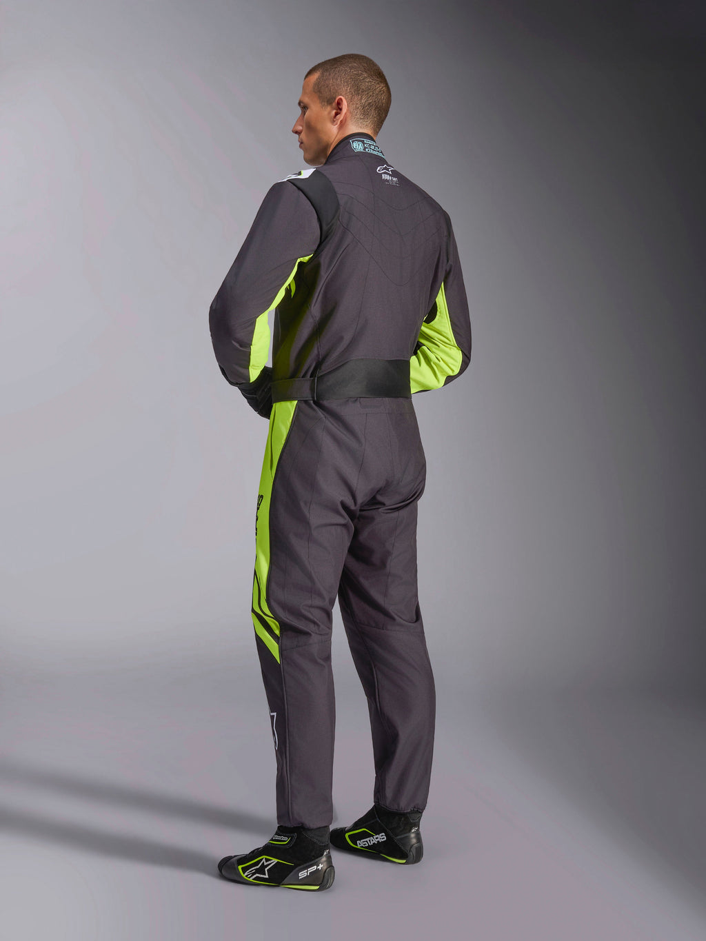 Traje Alpinestars KMX-9 V3 Graphic 3, mono de karting, negro y amarillo flúor, vista posterior del modelo mostrando el diseño de una sola pieza con detalles en amarillo flúor en los laterales y las axilas, paneles elásticos ergonómicos en la zona lumbar y cinturón ajustable, combinado con calzado de competición a juego.