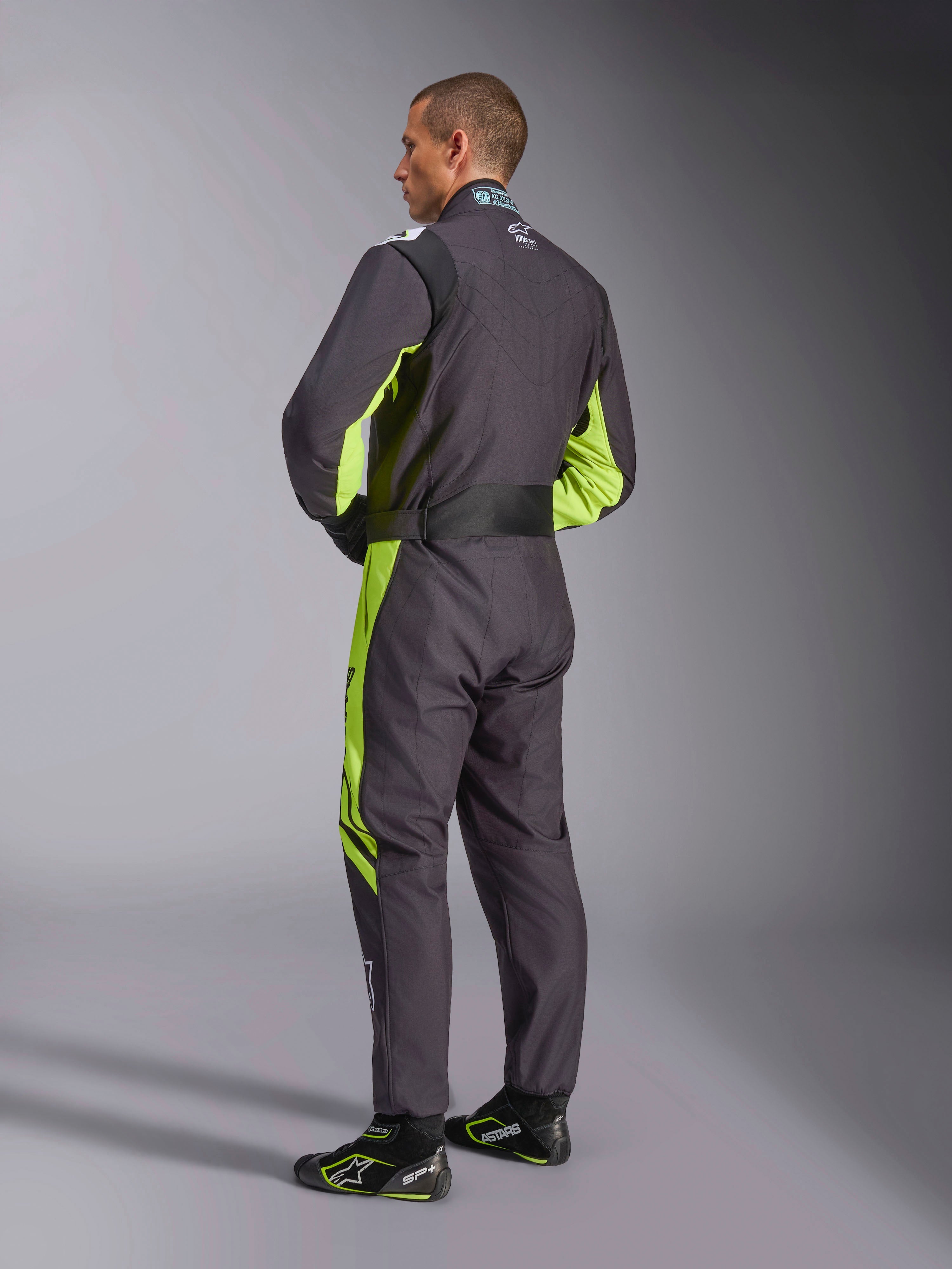 Traje Alpinestars KMX-9 V3 Graphic 3, mono de karting, negro y amarillo flúor, vista posterior del modelo mostrando el diseño de una sola pieza con detalles en amarillo flúor en los laterales y las axilas, paneles elásticos ergonómicos en la zona lumbar y cinturón ajustable, combinado con calzado de competición a juego.