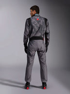 Alpinestars KMX-9 V3 Graphic 5 Suit, mono de karting, patrón de camuflaje en gris oscuro y negro en la parte superior, vista posterior que muestra los paneles elásticos y la marca Alpinestars, usado con guantes negros y calzado de carreras negro con detalles rojos, equipamiento profesional para automovilismo