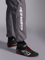 Mono Alpinestars KMX-9 V3 Graphic 5, mono de karting, gris oscuro, primer plano de la parte inferior de la pierna con el logotipo vertical de Alpinestars en blanco, combinado con calzado de carreras negro y rojo, material resistente para competición de karting