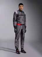 Mono Alpinestars KMX-9 V3 Graphic 5, traje de karting gris oscuro y negro con patrón de camuflaje, cinturón rojo con logo blanco, combinado con guantes y botas de carreras, equipamiento profesional de automovilismo para karting