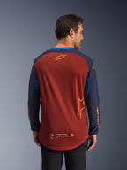Alpinestars Maxdura Dual Jersey en Rust Brown y Mood Indigo, vista desde atrás, con torso de malla transpirable, mangas azul oscuro con logotipos de Alpinestars en naranja y dobladillo trasero caído para mayor cobertura.