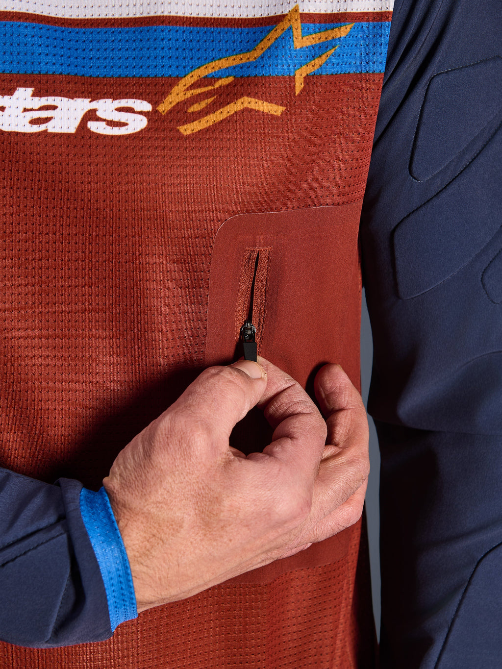 Detalle del jersey Alpinestars Maxdura Dual, torso de malla en color Rust Brown con bolsillo en el pecho con cremallera sin costuras, mangas Mood Indigo con acolchado integrado, detalle de jersey técnico de moto para aventura