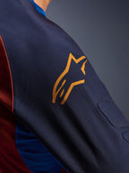 Alpinestars Maxdura Dual Jersey, primer plano de la manga en color Mood Indigo con un logotipo amarillo de Alpinestars, que muestra el acolchado de malla espaciadora integrado y el tejido de malla del torso en color Rust Brown, prenda técnica de motociclismo de aventura