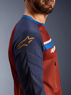 Alpinestars Maxdura Dual Jersey, Rust Brown y Mood Indigo, vista de perfil lateral que muestra las mangas acolchadas con el logotipo de la estrella amarilla, construcción del torso de malla con bolsillo en el pecho con cremallera, ropa técnica de motociclismo para conducción de aventura