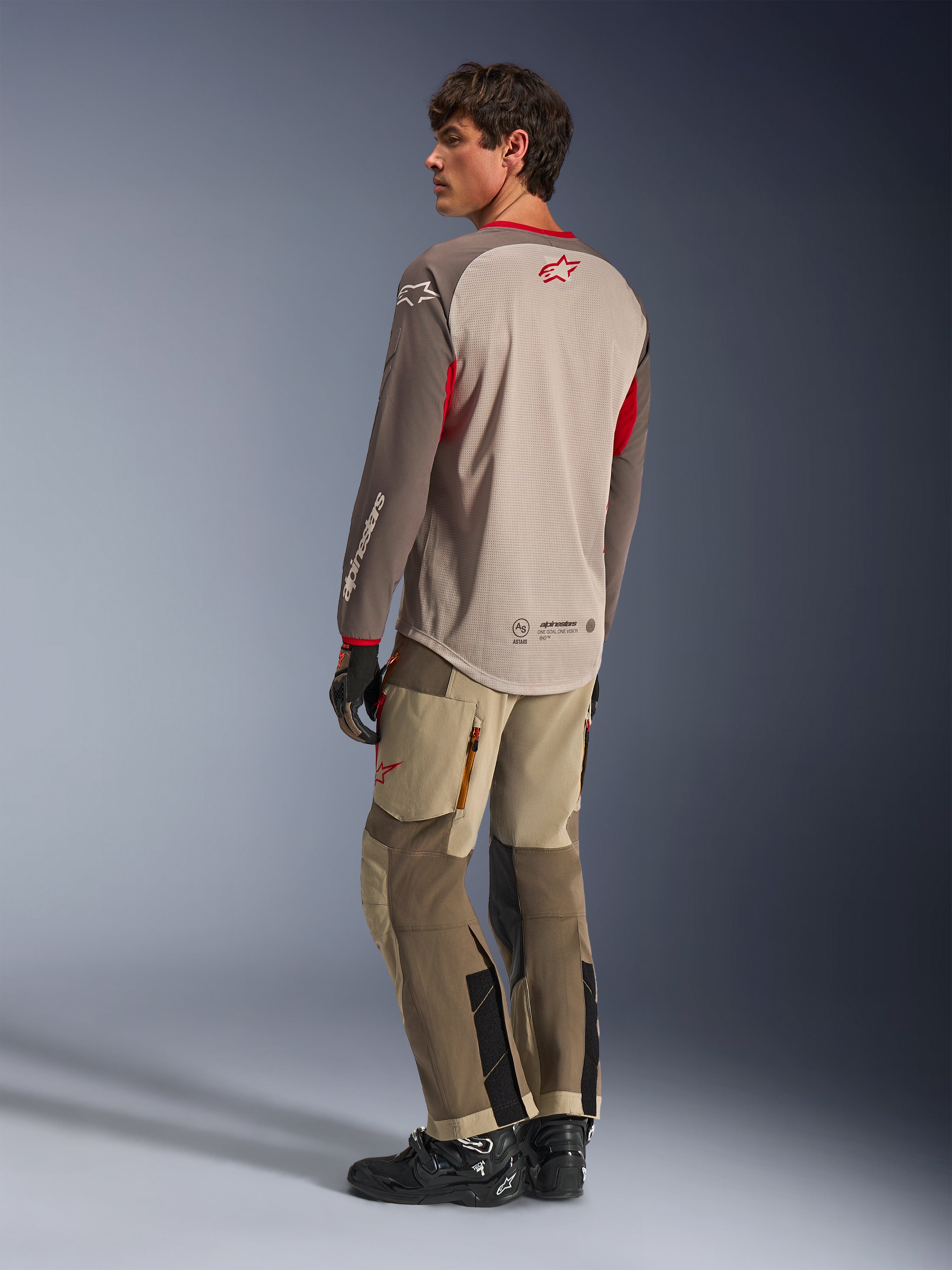 Alpinestars Maxdura Dual Jersey en color Aluminum Walnut, vista posterior del jersey de moto de aventura con torso de malla transpirable y detalles en rojo, combinado con pantalones técnicos de aventura a juego y botas negras