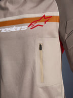 Alpinestars Maxdura Dual Jersey, Aluminum Walnut, detalle de primer plano del torso de malla, franja horizontal naranja y blanca con logotipo rojo, bolsillo con cremallera vertical en el pecho, equipamiento de aventura para motociclismo