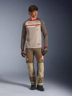 Jersey Alpinestars Maxdura Dual en Aluminum Walnut, jersey de motociclismo de aventura con torso de malla beige y mangas marrones, con cuello rojo y franja horizontal en el pecho con el logo de Alpinestars, combinado con pantalones de aventura y guantes a juego.