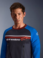 Alpinestars Maxdura Dual Jersey, gris oscuro y azul real, usado por un modelo masculino, con torso de malla, mangas azul real con acolchado integrado y bolsillos verticales con cremallera en el pecho con el logotipo de Alpinestars.
