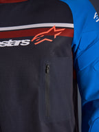 Alpinestars Maxdura Dual Jersey, primer plano de pecho y manga, gris oscuro y azul real, con bolsillo con cremallera en el pecho, torso de malla transpirable y acolchado integrado en las mangas, con el logotipo de Alpinestars sobre franjas rojas y blancas.