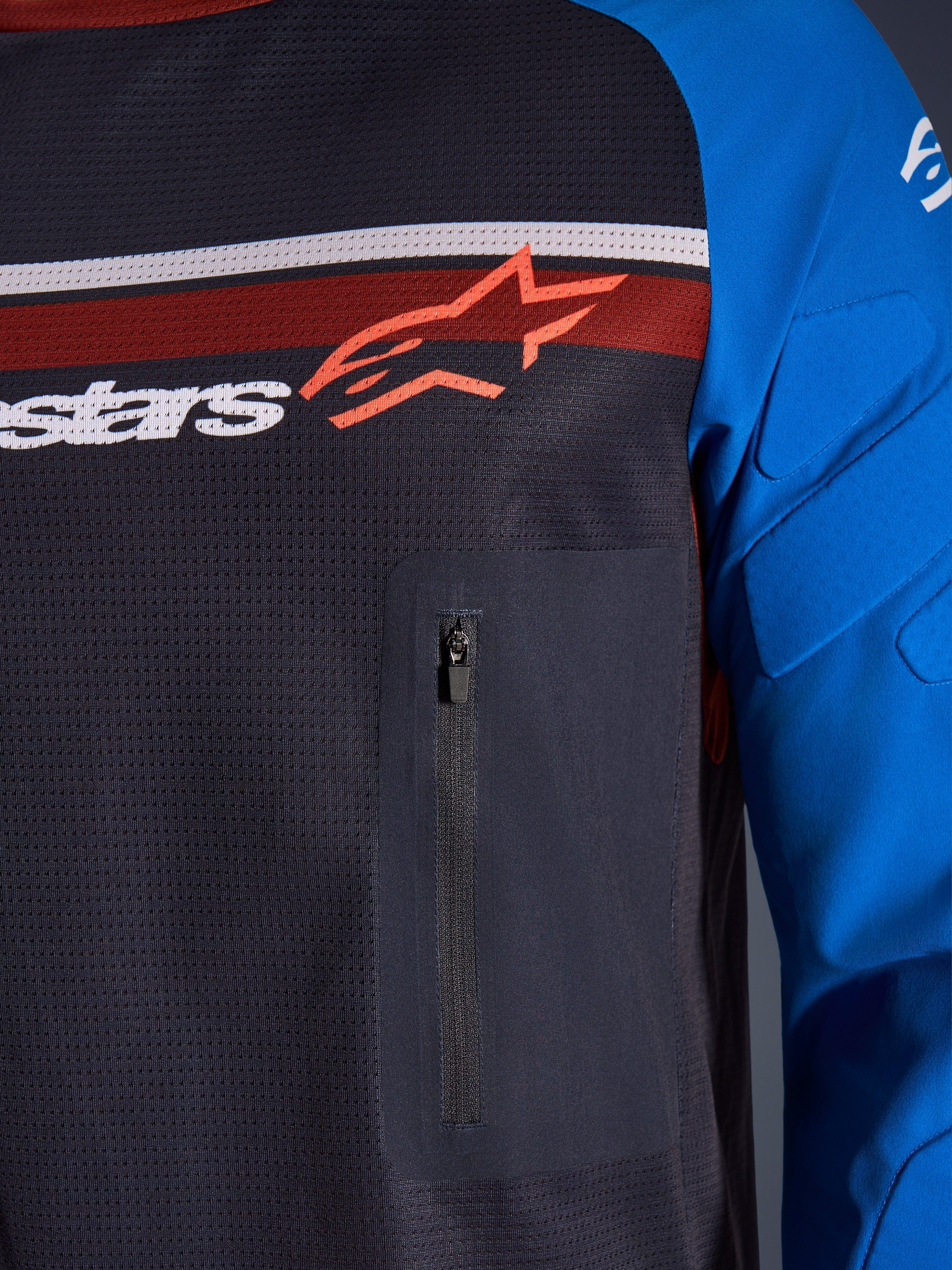 Alpinestars Maxdura Dual Jersey, primer plano de pecho y manga, gris oscuro y azul real, con bolsillo con cremallera en el pecho, torso de malla transpirable y acolchado integrado en las mangas, con el logotipo de Alpinestars sobre franjas rojas y blancas.