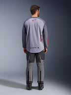 Modelo masculino desde atrás vistiendo la Alpinestars Maxdura Dual Jersey, jersey de aventura en gris medio y gris oscuro con detalles del logo en rojo, construcción de malla en la espalda, combinada con pantalones off-road grises a juego y botas negras