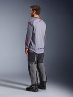 Hombre con el Jersey Alpinestars Maxdura Dual, gris claro con logotipos Alpinestars rojos, vista trasera que muestra el torso de malla y mangas largas, combinado con pantalones técnicos gris carbón y botas de moto negras