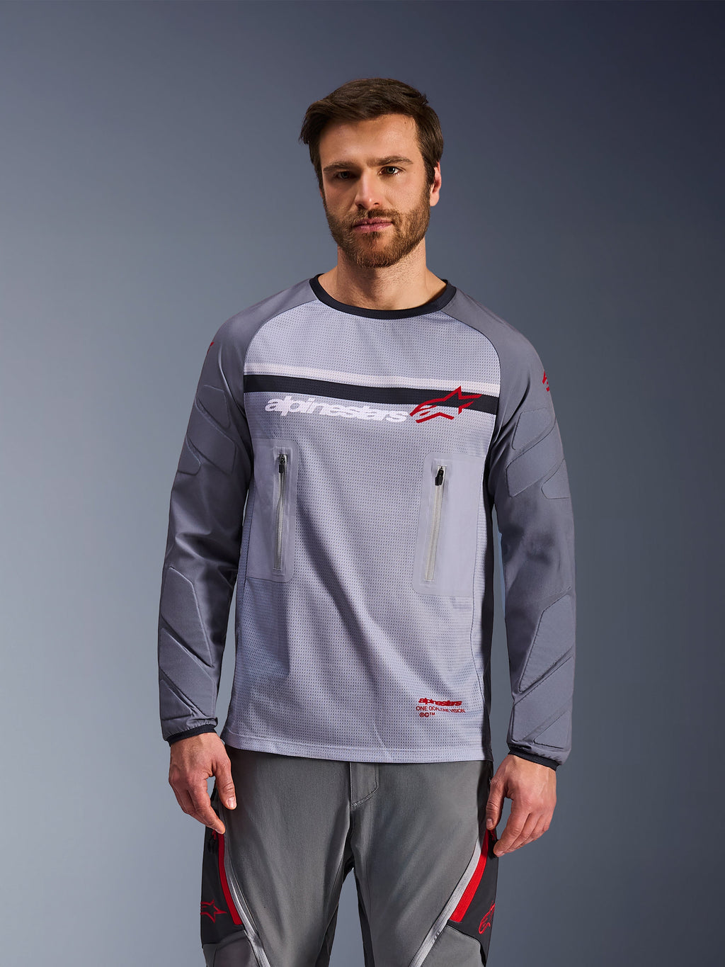Alpinestars Maxdura Dual Jersey, jersey de aventura para motocicleta, gris medio y gris oscuro, con torso de malla, bolsillos con cremallera en el pecho y mangas acolchadas resistentes a la abrasión, logo blanco y rojo en el pecho, equipamiento de aventura off-road