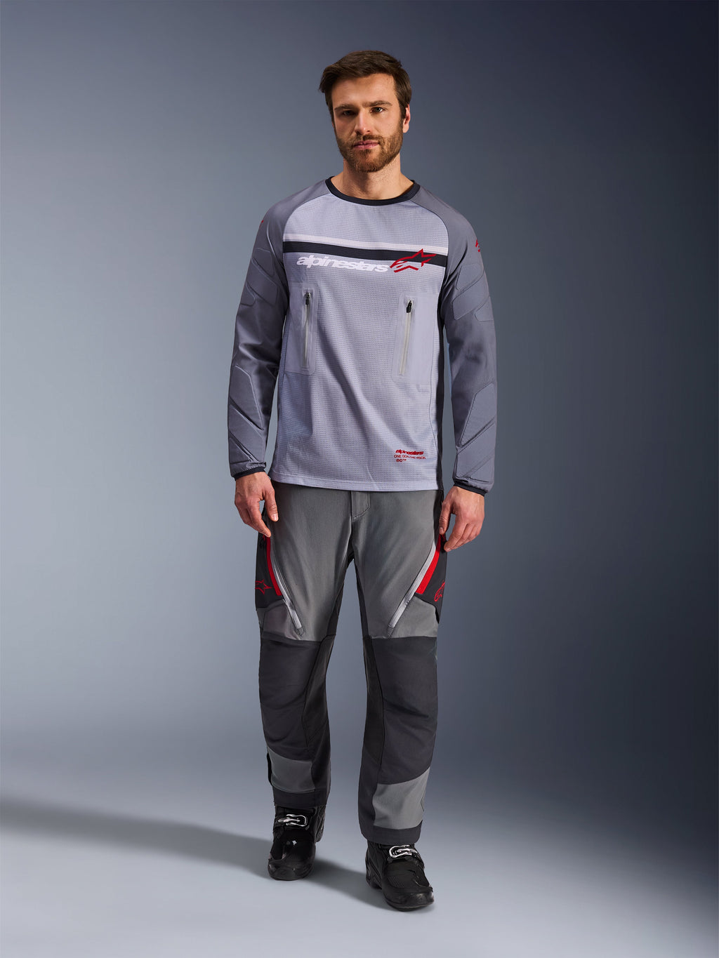 Alpinestars Maxdura Dual Jersey, gris medio y gris oscuro, jersey de motociclismo de aventura con torso de malla y bolsillos en el pecho con cremallera, mangas resistentes a la abrasión con acolchado integrado, combinado con pantalones técnicos grises a juego con detalles en rojo, equipamiento técnico de conducción off-road