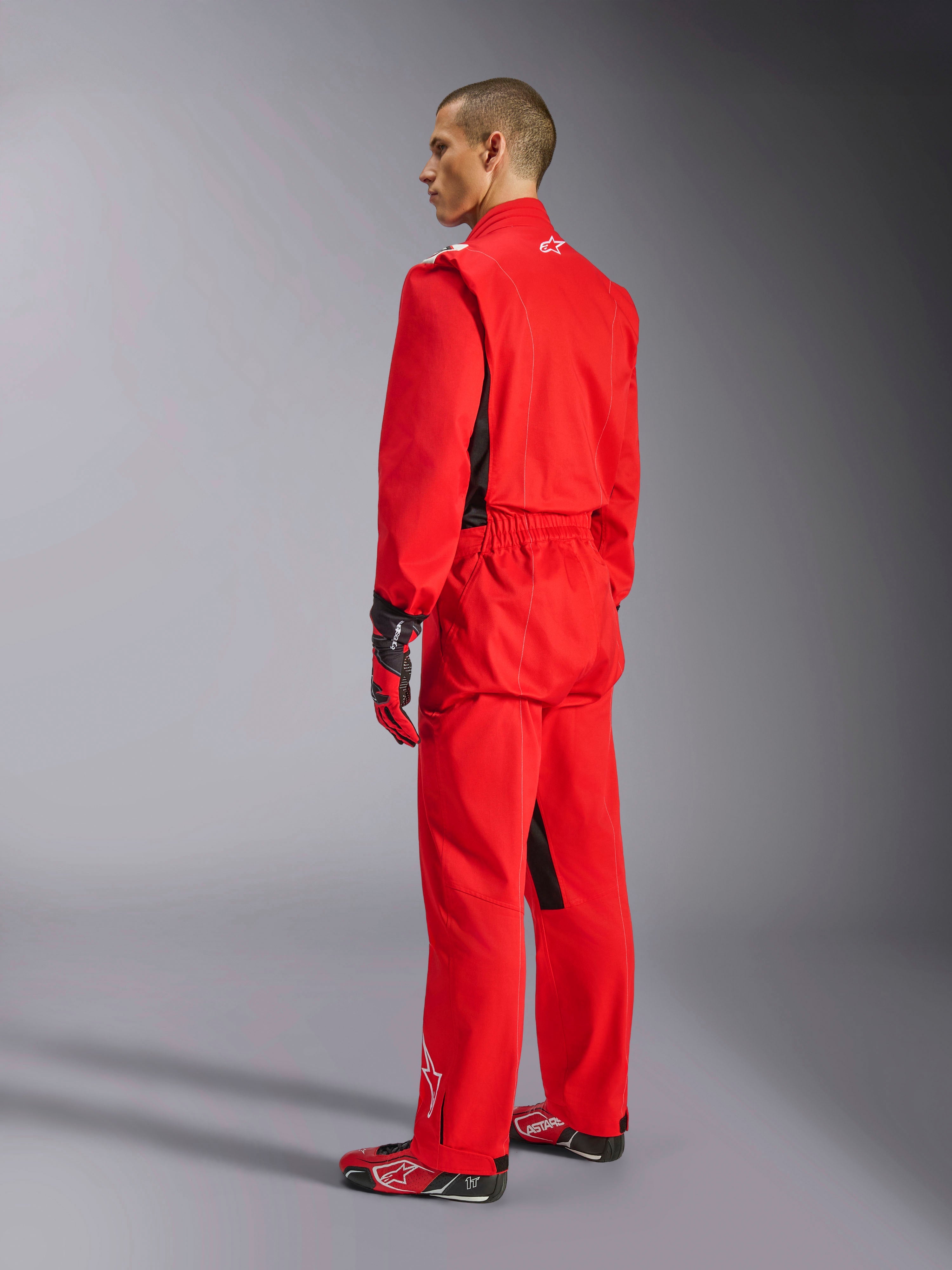 Alpinestars Kart Indoor V2 Suit, mono de karting rojo, vista trasera de tres cuartos en un modelo, usado con guantes rojos y calzado de competición a juego, construcción de sarga de poliéster y algodón de una sola capa, equipamiento profesional para karting en interiores