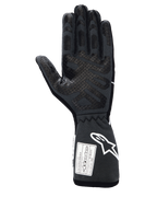Guantes Alpinestars Tech-1 Race V4, guantes profesionales de automovilismo, color negro y gris, vista de la palma con patrones de agarre de silicona en los dedos y la palma, puño extendido con logotipo blanco de Alpinestars y etiquetas de certificación FIA/SFI