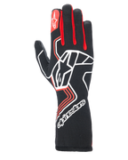 Guantes Alpinestars Tech-1 Race V4, guantes de carreras para automovilismo, negros con detalles rojos y blancos, gran logotipo de estrella blanca en el dorso, refuerzos rojos en los dedos, marca blanca en el puño largo extendido y patrones de diseño geométrico.