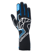 Guantes Alpinestars Tech-1 Race V4, guantes de carreras para automovilismo, negros con detalles en azul y blanco, con un gran logotipo blanco en el dorso, ribetes azules en los dedos y puño de guantelete extendido, diseño profesional resistente a las llamas para automovilismo