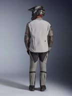 Chaqueta Alpinestars Nazca 3L GORE-TEX PRO, chaqueta de moto de aventura, gris oscuro y gris medio, vista trasera del piloto con equipamiento completo, combinada con pantalones a juego y casco de aventura negro, con logo rojo en la espalda y refuerzos de Superfabric en los codos, diseño textil duradero para turismo de aventura.