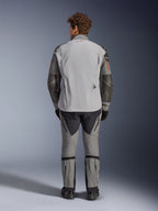 Chaqueta Alpinestars Nazca 3L GORE-TEX PRO, vista trasera, gris oscuro y gris medio, chaqueta de moto de aventura con construcción GORE-TEX, logo rojo en el cuello, detalles naranjas en las mangas, usada con pantalones de conducción a juego y guantes negros.