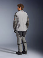 Chaqueta Alpinestars Nazca 3L GORE-TEX PRO, chaqueta de moto de aventura, en gris oscuro y gris medio, vista trasera, usada con pantalones de aventura a juego y botas negras, con refuerzos de Superfabric gris oscuro en las mangas, detalles de cremalleras en naranja y un pequeño logo rojo en la parte posterior del cuello.