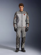 Chaqueta Alpinestars Nazca 3L GORE-TEX PRO, chaqueta de moto de aventura, gris oscuro y gris medio, vestida por un modelo con pantalones a juego y guantes negros, con detalles de cremalleras en naranja y logotipo rojo en el pecho, equipo de protección técnica para conducción extrema