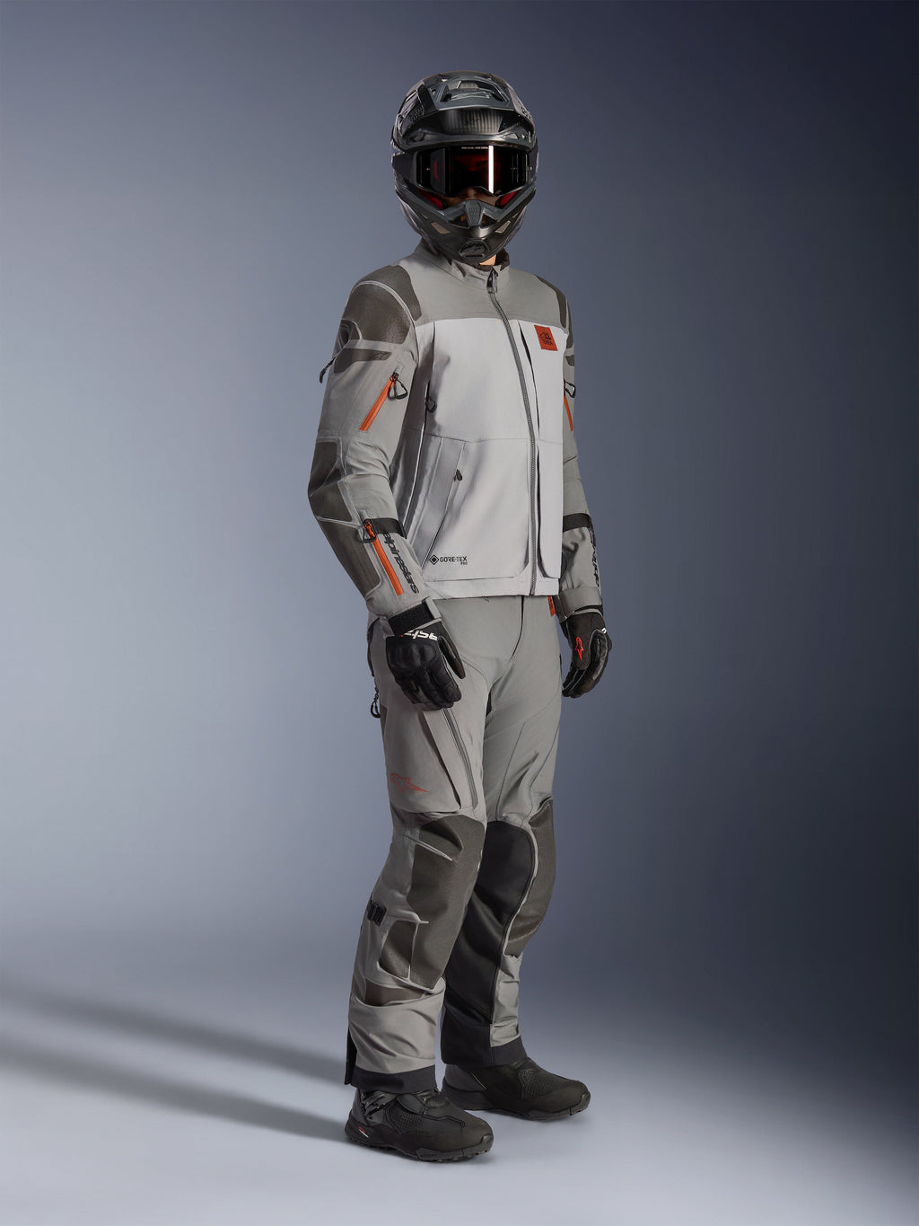 Chaqueta Alpinestars Nazca 3L GORE-TEX PRO, chaqueta de moto adventure, gris oscuro y gris medio, usada como un conjunto completo con pantalones de aventura a juego, con detalles en naranja y refuerzos Superfabric, incluye casco y guantes de aventura negros, indumentaria técnica para touring y conducción off-road