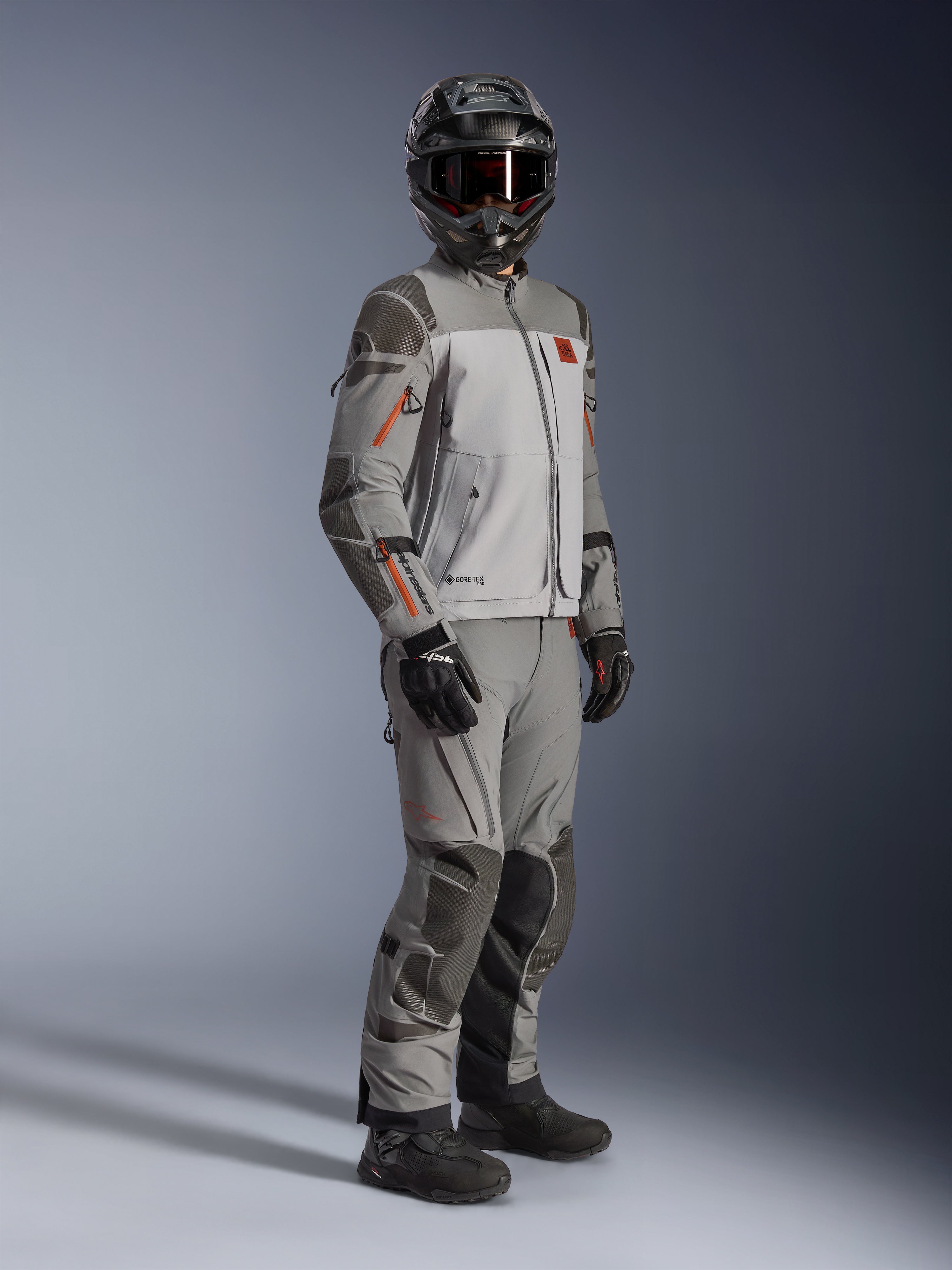 Chaqueta Alpinestars Nazca 3L GORE-TEX PRO, chaqueta de moto adventure, gris oscuro y gris medio, usada como un conjunto completo con pantalones de aventura a juego, con detalles en naranja y refuerzos Superfabric, incluye casco y guantes de aventura negros, indumentaria técnica para touring y conducción off-road